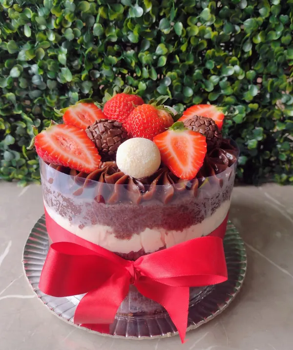 Bolo confeitado de brigadeiro com leite ninho e morangos, com laço vermelho